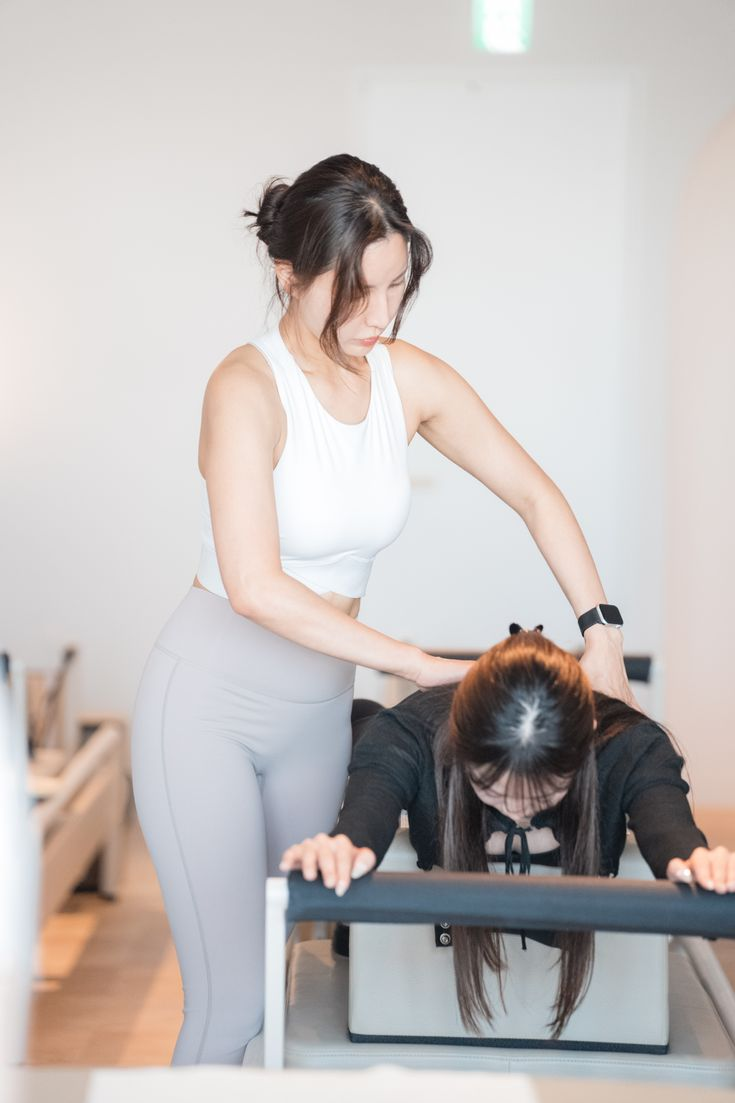 A Komi studio instructor guiding a student through a reformer Pilates exercise